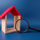 The image, featuring a small wooden house model and a magnifying glass on a blue background The image, featuring a small wooden house model and a magnifying glass on a blue background - PhotoDune Item for Sale