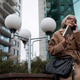 Older woman in a brown coat talking on the phone while sitting near modern buildings on a cloudy day Older woman in a brown coat talking on the phone while sitting near modern buildings on a cloudy day - PhotoDune Item for Sale