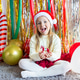Smiling young girl in festive outfit sitting on rug with holiday decorations Smiling young girl in festive outfit sitting on rug with holiday decorations - PhotoDune Item for Sale