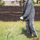 An elderly man in workwear mows grass and dandelions with an electric mower An elderly man in workwear mows grass and dandelions with an electric mower - PhotoDune Item for Sale