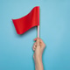 Hand holding a small red flag against a blue background Hand holding a small red flag against a blue background - PhotoDune Item for Sale