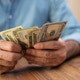 Close-up of a person holding and counting US dollar bills at a wooden table. Concept of financial Close-up of a person holding and counting US dollar bills at a wooden table. Concept of financial - PhotoDune Item for Sale