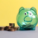Green transparent piggy bank standing next to stacks of coins for savings and investment concept Green transparent piggy bank standing next to stacks of coins for savings and investment concept - PhotoDune Item for Sale