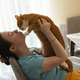A brunette caucasian woman kisses and plays with a ginger domestic cat while sitting in a kitchen A brunette caucasian woman kisses and plays with a ginger domestic cat while sitting in a kitchen - PhotoDune Item for Sale