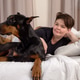 Happy woman relaxing on bed with her loyal Doberman Pinscher companion Happy woman relaxing on bed with her loyal Doberman Pinscher companion - PhotoDune Item for Sale