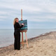 Young woman painting seascape on easel at beach during cloudy day Young woman painting seascape on easel at beach during cloudy day - PhotoDune Item for Sale