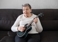 Elderly woman 70+ sits on the couch at home and plays the ukulele Elderly woman 70+ sits on the couch at home and plays the ukulele - PhotoDune Item for Sale