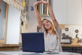 Young relaxed woman sitting in kitchen with laptop in front of her stretching her arms above. Young relaxed woman sitting in kitchen with laptop in front of her stretching her arms above. - PhotoDune Item for Sale
