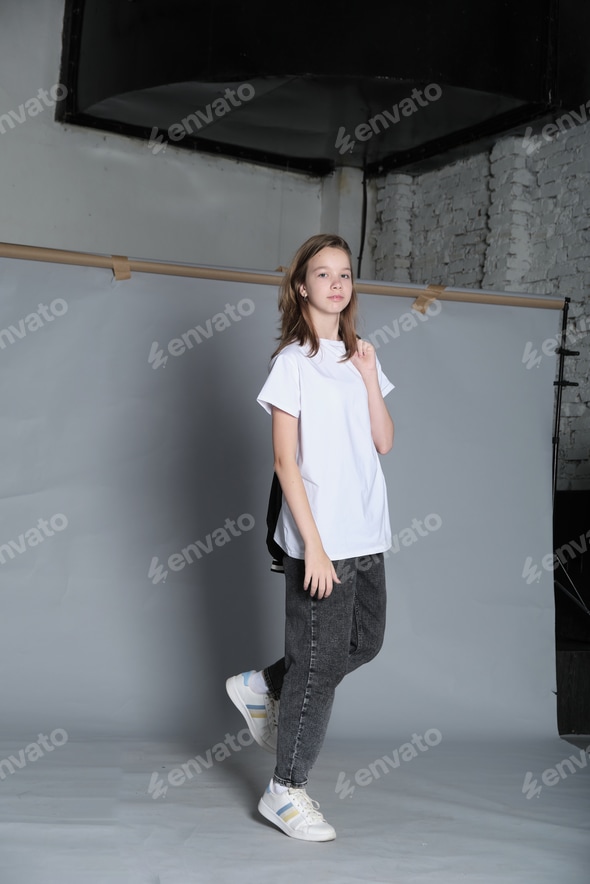 A girl poses casually, wearing a white t-shirt and jeans with a