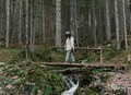 Side view of girl crossing wooden footbridge over creek in forest in autumn Side view of girl crossing wooden footbridge over creek in forest in autumn - PhotoDune Item for Sale