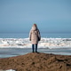 Woman stands on beach looking at ocean waves on a clear day with ice in the distance Woman stands on beach looking at ocean waves on a clear day with ice in the distance - PhotoDune Item for Sale
