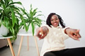 African woman sitting near greenery at home and show two fingers to camera. African woman sitting near greenery at home and show two fingers to camera. - PhotoDune Item for Sale