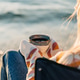 Closeup of a woman sitting in chair on winter sea shore in a cozy sweater and holding hot cup of Closeup of a woman sitting in chair on winter sea shore in a cozy sweater and holding hot cup of - PhotoDune Item for Sale