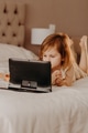 Toddler girl lying in bedroom, using laptop tablet pad gadget, watching with focused face Toddler girl lying in bedroom, using laptop tablet pad gadget, watching with focused face - PhotoDune Item for Sale
