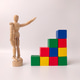 Wooden artist's mannequin posed next to a structure made of colorful wooden toy blocks Wooden artist's mannequin posed next to a structure made of colorful wooden toy blocks - PhotoDune Item for Sale