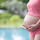 Close-up of a pregnant woman in a red patterned outfit gently cradling her belly near a pool. Close-up of a pregnant woman in a red patterned outfit gently cradling her belly near a pool. - PhotoDune Item for Sale
