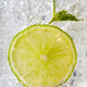 Macro photo of a piece of lime and mint leaf in a glass with ice and bubbles. Cold summer drink Macro photo of a piece of lime and mint leaf in a glass with ice and bubbles. Cold summer drink - PhotoDune Item for Sale