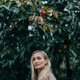 A beautiful elegant blonde woman in a coat stands in the garden under a ripe persimmon tree. A beautiful elegant blonde woman in a coat stands in the garden under a ripe persimmon tree. - PhotoDune Item for Sale