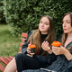 Young girlfriends gossiping over coffee on park bench with green leafy background Young girlfriends gossiping over coffee on park bench with green leafy background - PhotoDune Item for Sale