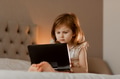 Toddler girl sitting in bedroom, using laptop tablet pad gadget, watching with focused face Toddler girl sitting in bedroom, using laptop tablet pad gadget, watching with focused face - PhotoDune Item for Sale