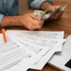 Man in denim shirt counting cash while examining tax forms on a wooden desk. Man in denim shirt counting cash while examining tax forms on a wooden desk. - PhotoDune Item for Sale