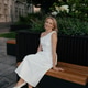 Smiling woman in white dress sitting on modern wooden bench in city park Smiling woman in white dress sitting on modern wooden bench in city park - PhotoDune Item for Sale