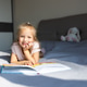 Smiling young girl reading a book while lying on a bed at home Smiling young girl reading a book while lying on a bed at home - PhotoDune Item for Sale