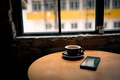 A cup of coffee near window with smartphone on the table A cup of coffee near window with smartphone on the table - PhotoDune Item for Sale