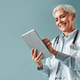 Beautiful female medic working with a digital tablet on a blue background. Family doctor. Beautiful female medic working with a digital tablet on a blue background. Family doctor. - PhotoDune Item for Sale