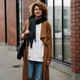 Stylish woman with curly hair walking in the city wearing a brown coat and jeans Stylish woman with curly hair walking in the city wearing a brown coat and jeans - PhotoDune Item for Sale