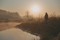 Woman walking through a meadow by a pond in the foggy morning Woman walking through a meadow by a pond in the foggy morning - PhotoDune Item for Sale