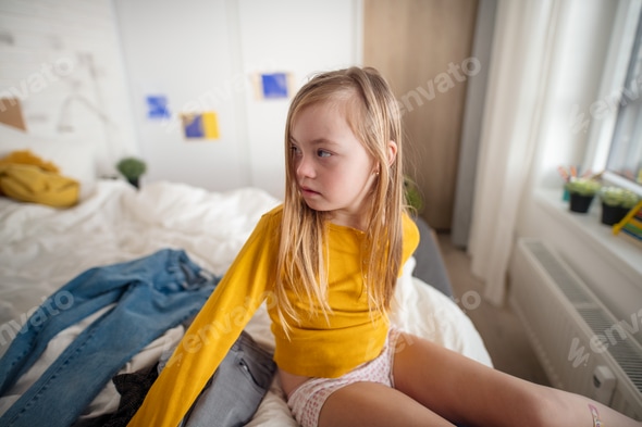 Sad little girl with Down syndrome getting dressed at home. Stock Photo by halfpoint Sad little girl with Down syndrome getting dressed at home. Stock Photo by halfpoint