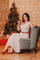 Smart brunette girl in white dress with red accessories sitting above Christmas tree with glass Smart brunette girl in white dress with red accessories sitting above Christmas tree with glass - PhotoDune Item for Sale