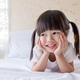 Portrait adorable little girl with pigtails smile brightly while lying on a white bed Portrait adorable little girl with pigtails smile brightly while lying on a white bed - PhotoDune Item for Sale