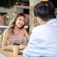 Asian woman smiling and talking to a male friend while sitting at wooden table in a cafe or canteen. Asian woman smiling and talking to a male friend while sitting at wooden table in a cafe or canteen. - PhotoDune Item for Sale