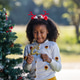 A happy child wearing reindeer antlers decorates a Christmas tree with festive ornaments outdoors. A happy child wearing reindeer antlers decorates a Christmas tree with festive ornaments outdoors. - PhotoDune Item for Sale