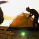 Silhouette of young bearded man sets up a tent at campsite on the lake shore Silhouette of young bearded man sets up a tent at campsite on the lake shore - PhotoDune Item for Sale
