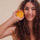 Young woman with curly hair holds a fresh orange slice near her face Young woman with curly hair holds a fresh orange slice near her face - PhotoDune Item for Sale