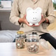 Close up office worker man holding a piggy bank aside coin glass jars sitting on sofa in living room Close up office worker man holding a piggy bank aside coin glass jars sitting on sofa in living room - PhotoDune Item for Sale