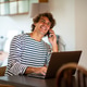 Smiling young man sitting at home talking on cell phone while working on laptop Smiling young man sitting at home talking on cell phone while working on laptop - PhotoDune Item for Sale