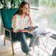 A business woman in a white shirt sits in a chair by the window using a laptop to work. A business woman in a white shirt sits in a chair by the window using a laptop to work. - PhotoDune Item for Sale