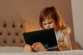 Toddler girl lying on bed in modern room, using laptop tablet pad gadget, watching with focused face Toddler girl lying on bed in modern room, using laptop tablet pad gadget, watching with focused face - PhotoDune Item for Sale