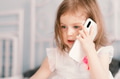 Cute little girl sitting with smartphone in bedroom with thinking look and focusing on talk. Cute little girl sitting with smartphone in bedroom with thinking look and focusing on talk. - PhotoDune Item for Sale