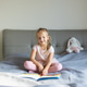 Young girl reading a book while sitting on a bed in a brightly lit bedroom. Peaceful morning moment Young girl reading a book while sitting on a bed in a brightly lit bedroom. Peaceful morning moment - PhotoDune Item for Sale