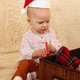 Little girl in Santa Claus red hat is playing with Christmas decorations on a beige plaid. Little girl in Santa Claus red hat is playing with Christmas decorations on a beige plaid. - PhotoDune Item for Sale