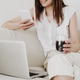 Cropped image of young female using mobile phone and laptop while drinking coffee on a couch. Cropped image of young female using mobile phone and laptop while drinking coffee on a couch. - PhotoDune Item for Sale