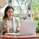 Pretty asian woman wearing earphone open palms looking at laptop as sitting at table in garden cafe. Pretty asian woman wearing earphone open palms looking at laptop as sitting at table in garden cafe. - PhotoDune Item for Sale