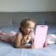 Young girl using pink drawing tablet while lying on bed at home Young girl using pink drawing tablet while lying on bed at home - PhotoDune Item for Sale