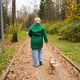 Walking woman with small dog on forest park path. Outdoor pet exercise supports health, stress Walking woman with small dog on forest park path. Outdoor pet exercise supports health, stress - PhotoDune Item for Sale