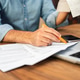 Man in a denim shirt calculating taxes with receipts and forms on a wooden desk. Man in a denim shirt calculating taxes with receipts and forms on a wooden desk. - PhotoDune Item for Sale